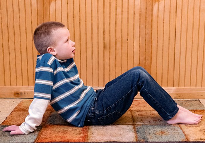 Young child sitting on the floor, leaning back, and supporting himself with his arms