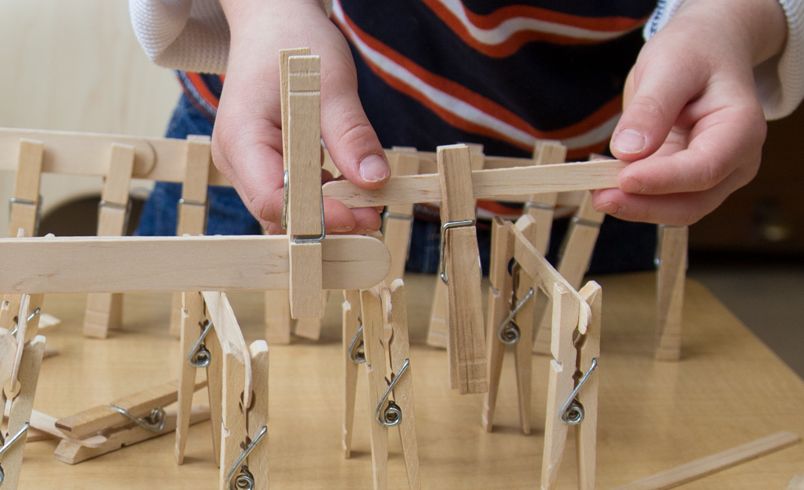 a child’s hands constructing something out of clothspins and ice cream sticks