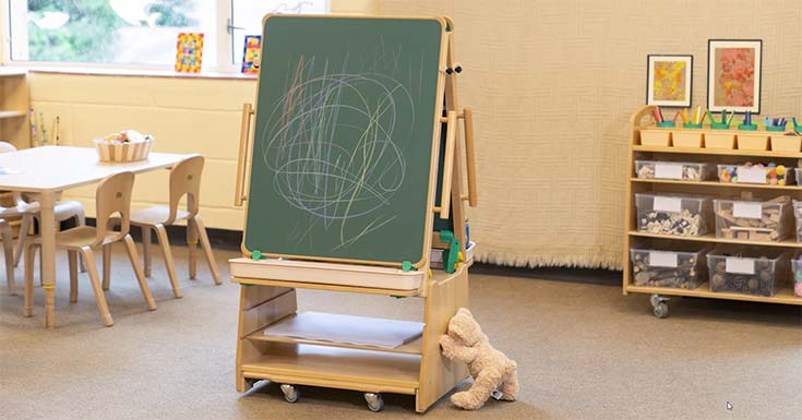 A teddybear is pushing an easel through a nursery room